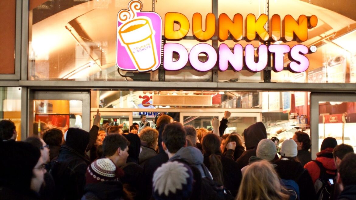 A crowd of people standing outside of dunkin donuts.