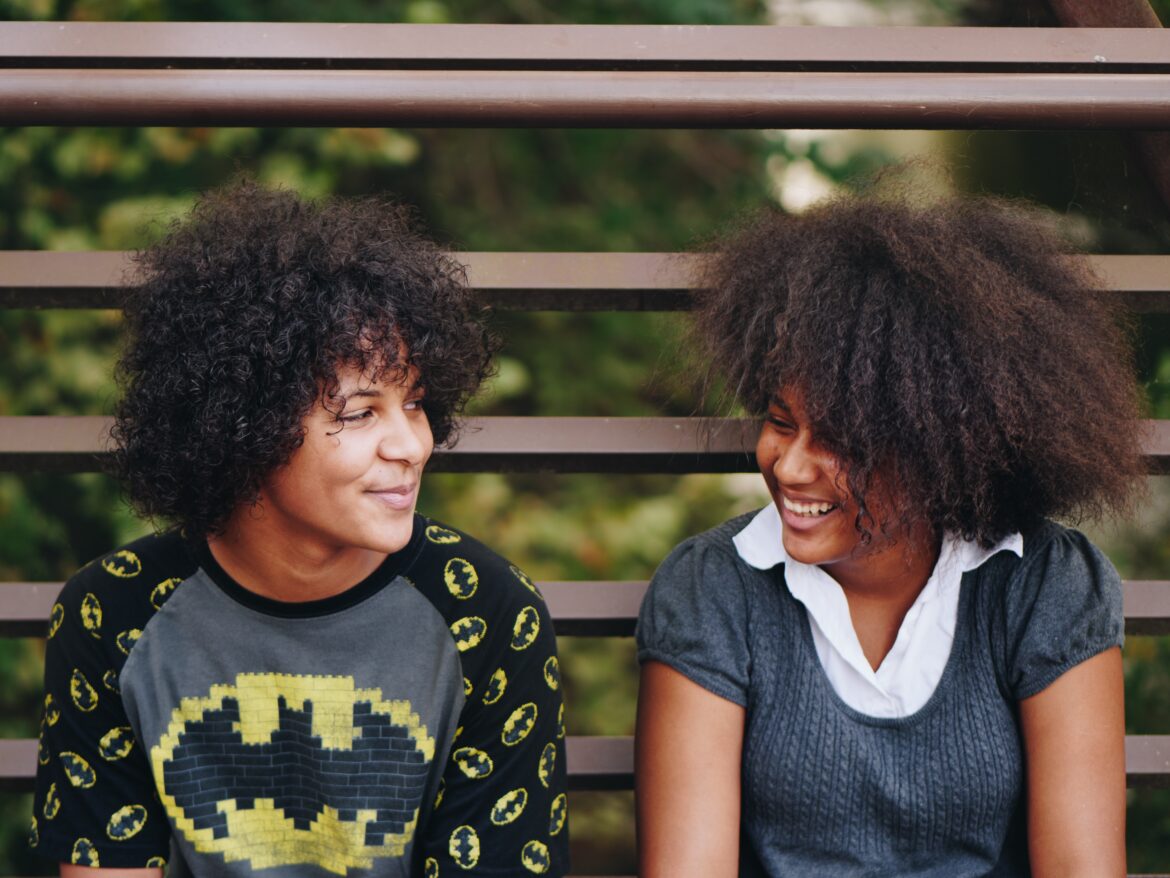 Two women sitting on a bench smiling at each other.