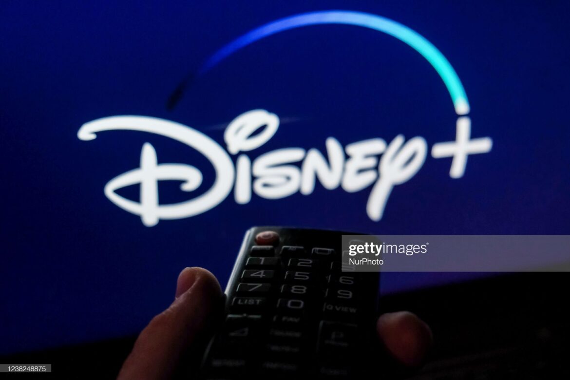 A person holding a remote control in front of the disney logo.
