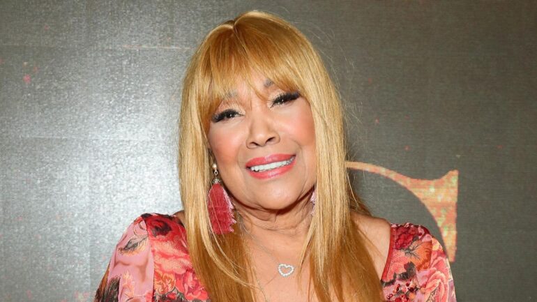 A woman with long blonde hair and pink earrings.